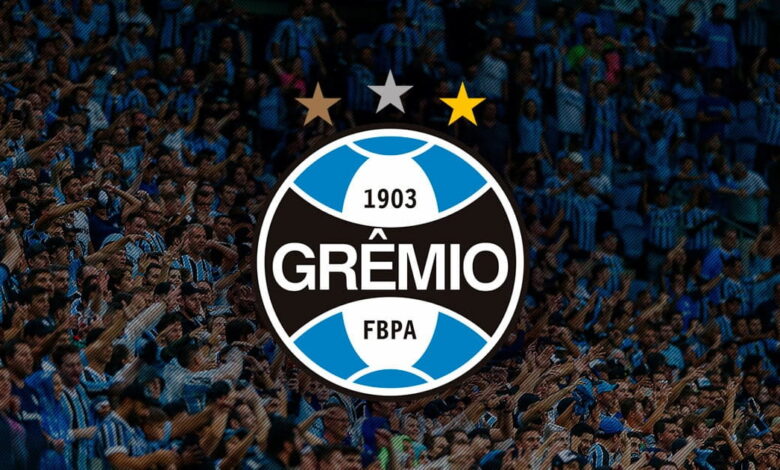 Escudo do Grêmio com torcedores ao fundo